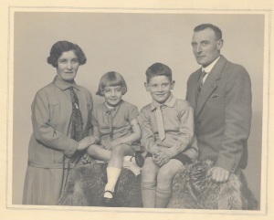 A Studio photograph from the 1920s featuring a white family of mother, father, son and daughter in formal clothes, smiling.
