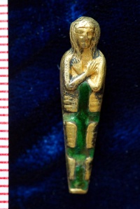 Miniature gold charm of an Egyptian mummy, with arms crossed across the chest, inlaid with green enamel stripes or bandages. 
