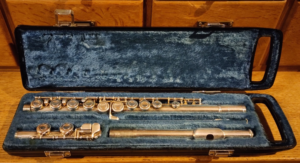 Silver plated Yamaha flute, disassembled, inside an open case with blue furry fabric lining. 