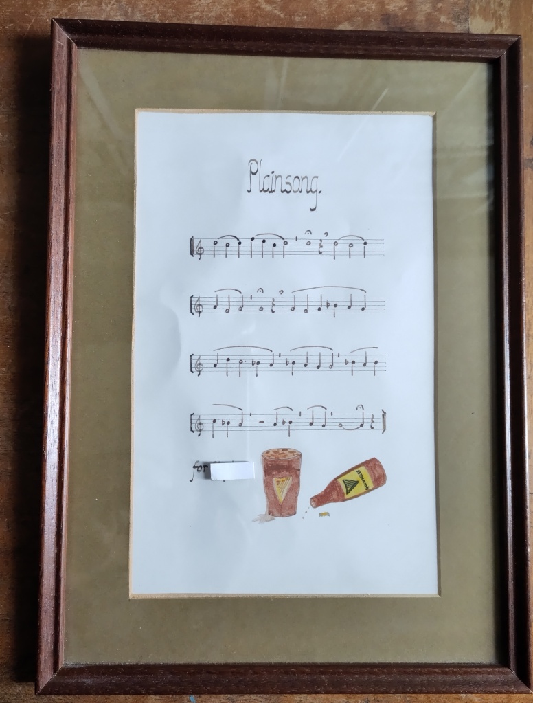 A framed, handwritten piece of music entitled Plainsong, with an illustration of a bottle and a pint of Guinness.