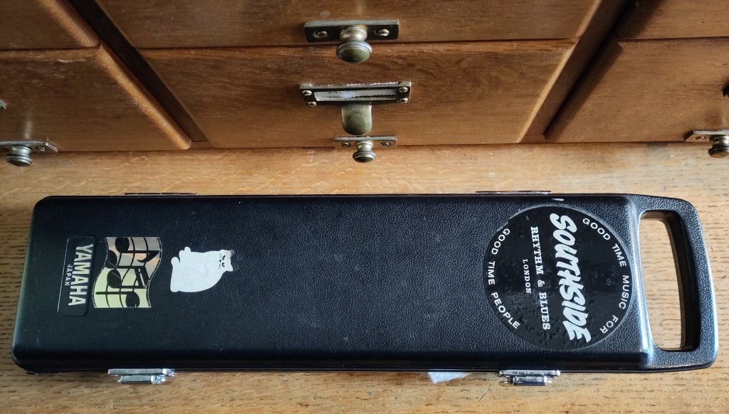 A black flute case with a handle, closed, with stickers of a white cat, some music notes and the band Southside, which reads "Good time music for good time people."