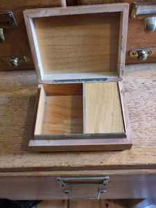 Wooden Music box with lid open, showing an empty compartment on the left side, and the right side covered with a wooden lid. 